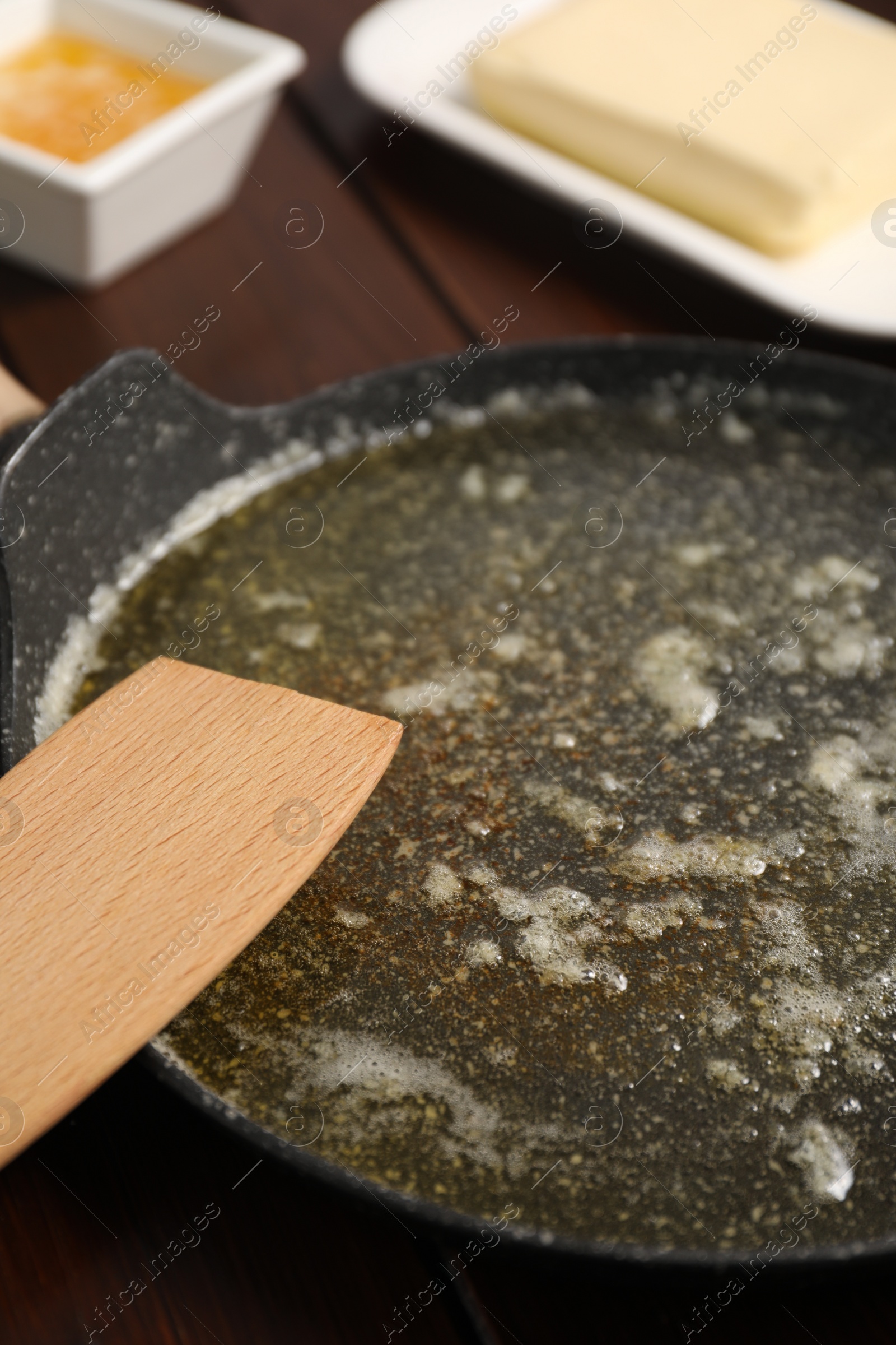 Photo of Melted butter in frying pan and spatula on wooden table, closeup