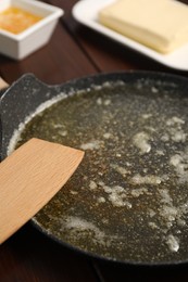 Photo of Melted butter in frying pan and spatula on wooden table, closeup