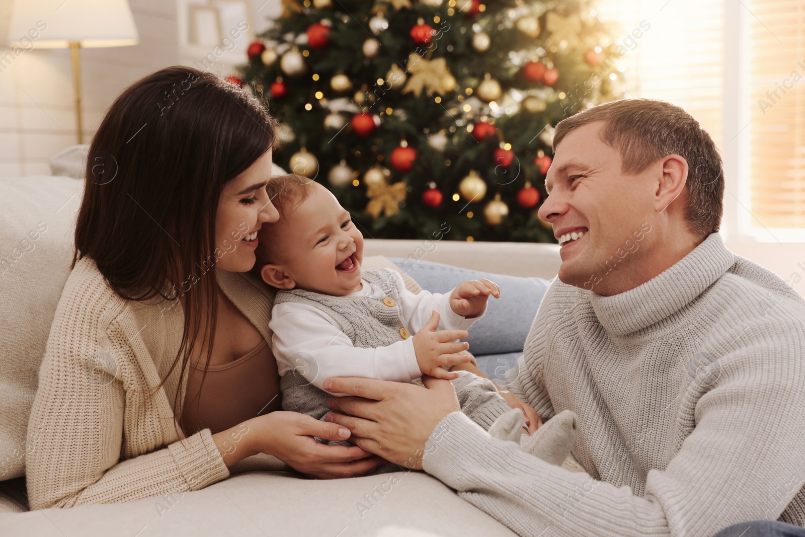 Photo of Happy couple with cute baby in living room decorated for Christmas