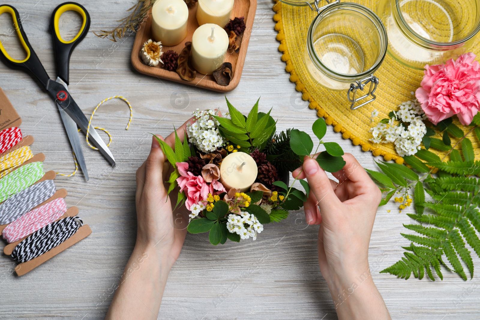 Photo of Woman making floral composition with candle at wooden table, top view. Master class in handmade craft