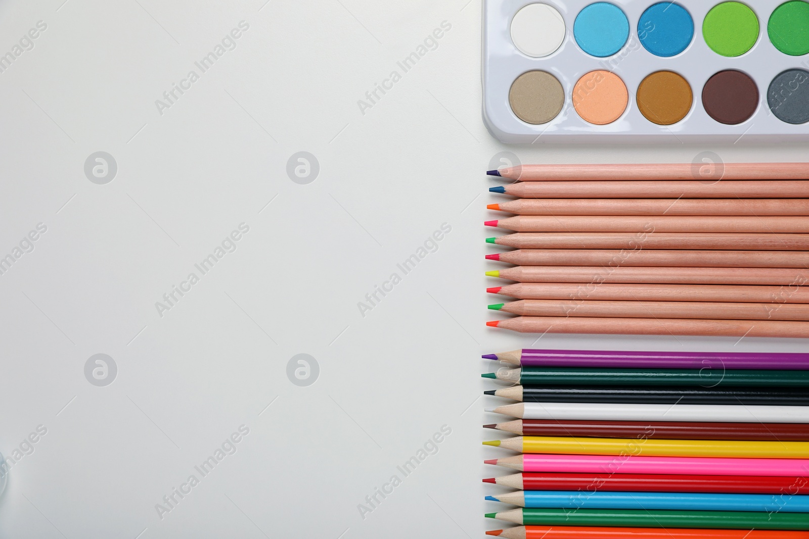 Photo of Watercolor palette and colorful pencils on white background, flat lay. Space for text