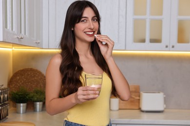 Photo of Beautiful woman taking vitamin pill in kitchen