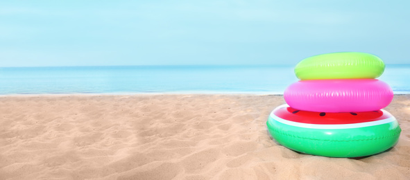 Pile of colorful inflatable rings on sand near sea, space for text. Banner design