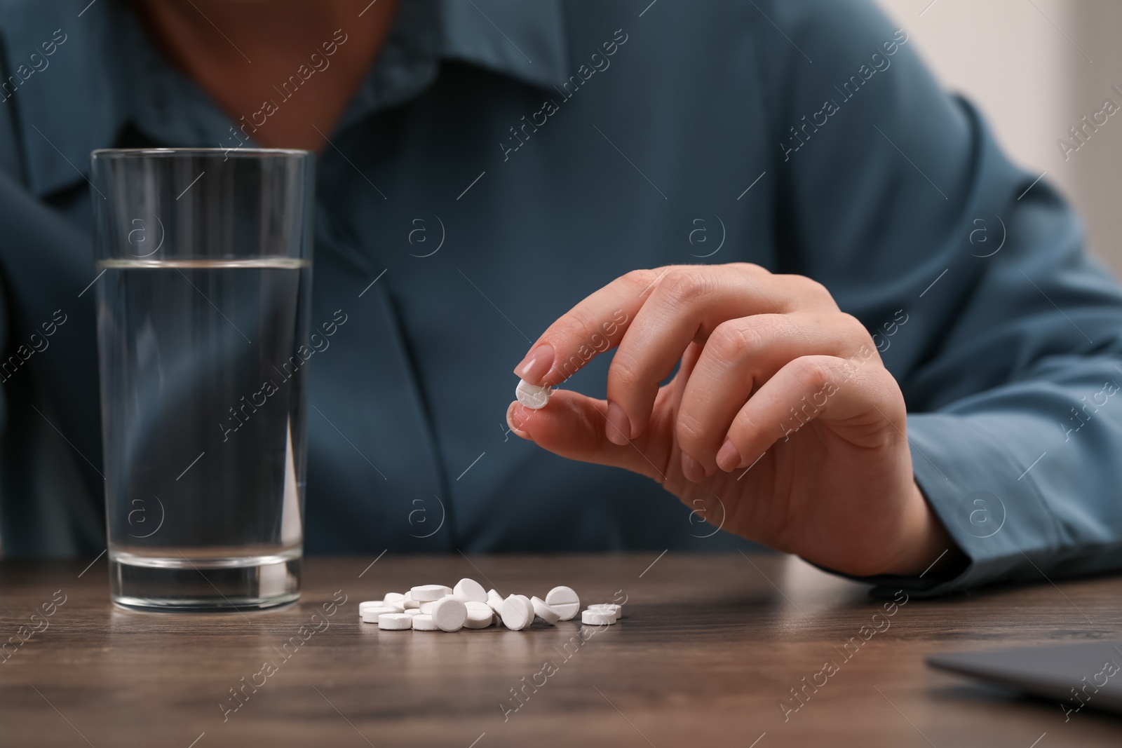 Photo of Woman with antidepressant pills and glass of water at wooden table, closeup