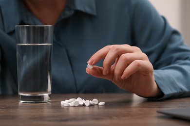 Photo of Woman with antidepressant pills and glass of water at wooden table, closeup