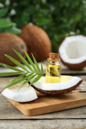 Photo of Bottle of organic coconut cooking oil, fruit pieces and leaf on wooden table