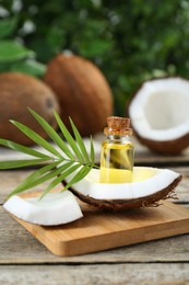 Bottle of organic coconut cooking oil, fruit pieces and leaf on wooden table