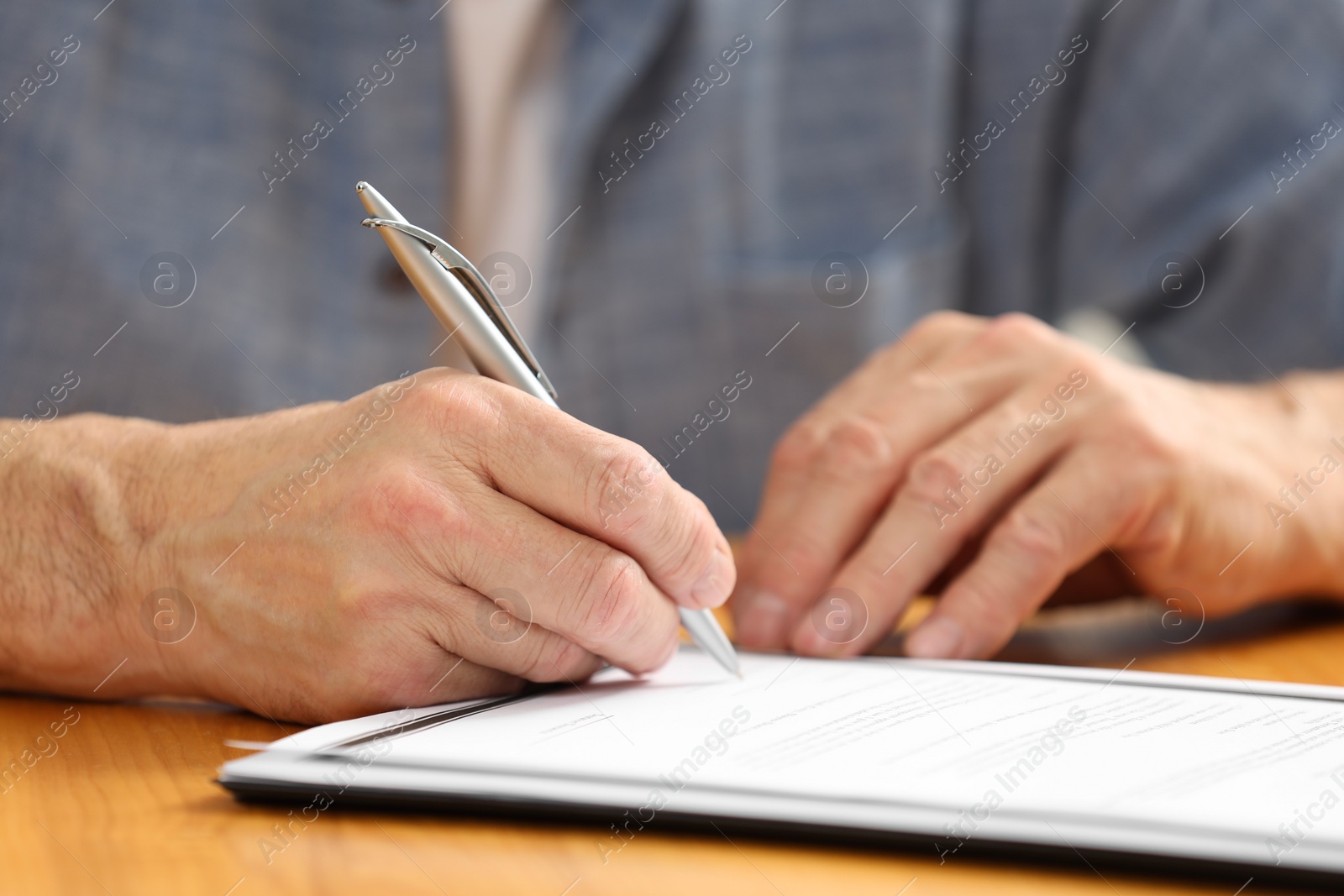 Photo of Senior man signing Last Will and Testament at wooden table, closeup