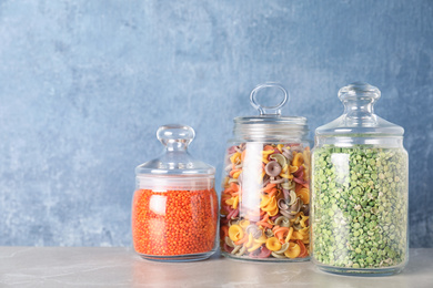 Photo of Jars with different cereals on grey marble table against light blue background