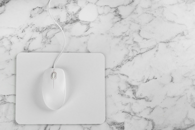 Photo of Modern wired optical mouse and pad on white marble table, top view. Space for text