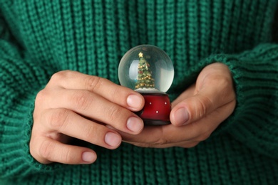 Woman wearing green sweater holding snow globe with Christmas tree, closeup