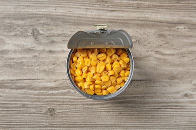 Photo of Open tin can of corn kernels on wooden background, top view