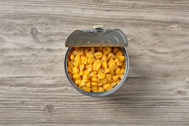 Open tin can of corn kernels on wooden background, top view