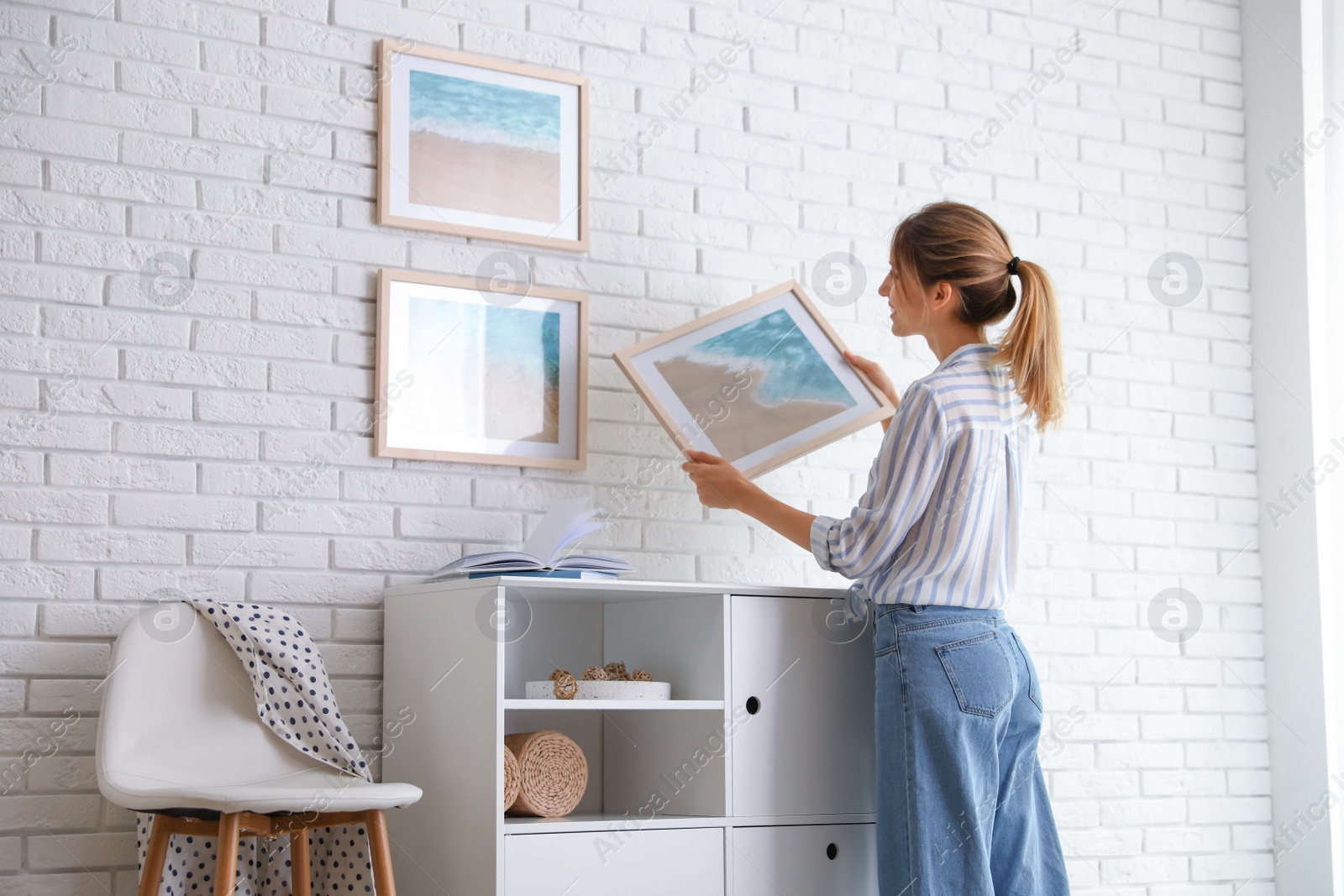 Photo of Decorator hanging picture on white brick wall in room. Interior design