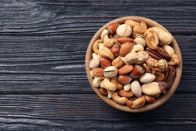 Bowl with organic mixed nuts on wooden background, top view. Space for text