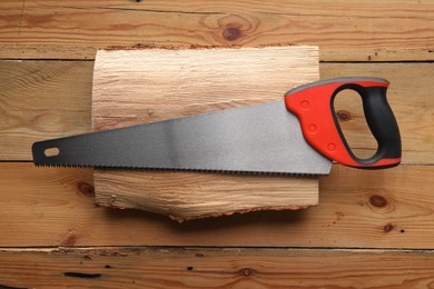 Saw with colorful handle and log on wooden background, top view