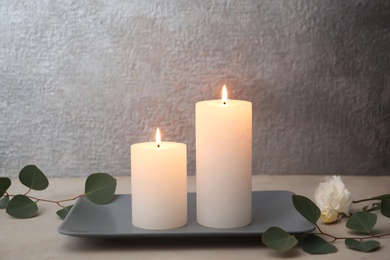 Photo of Candles with floral decor on table against color background