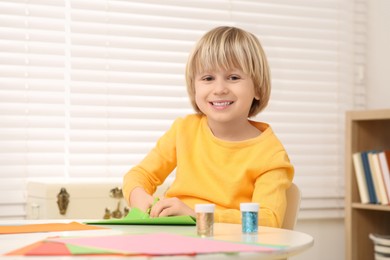 Photo of Cute little boy cutting green paper at desk in room. Home workplace