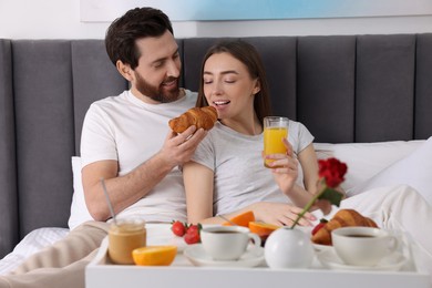 Photo of Healthy breakfast. Happy husband feeding his wife on bed at home