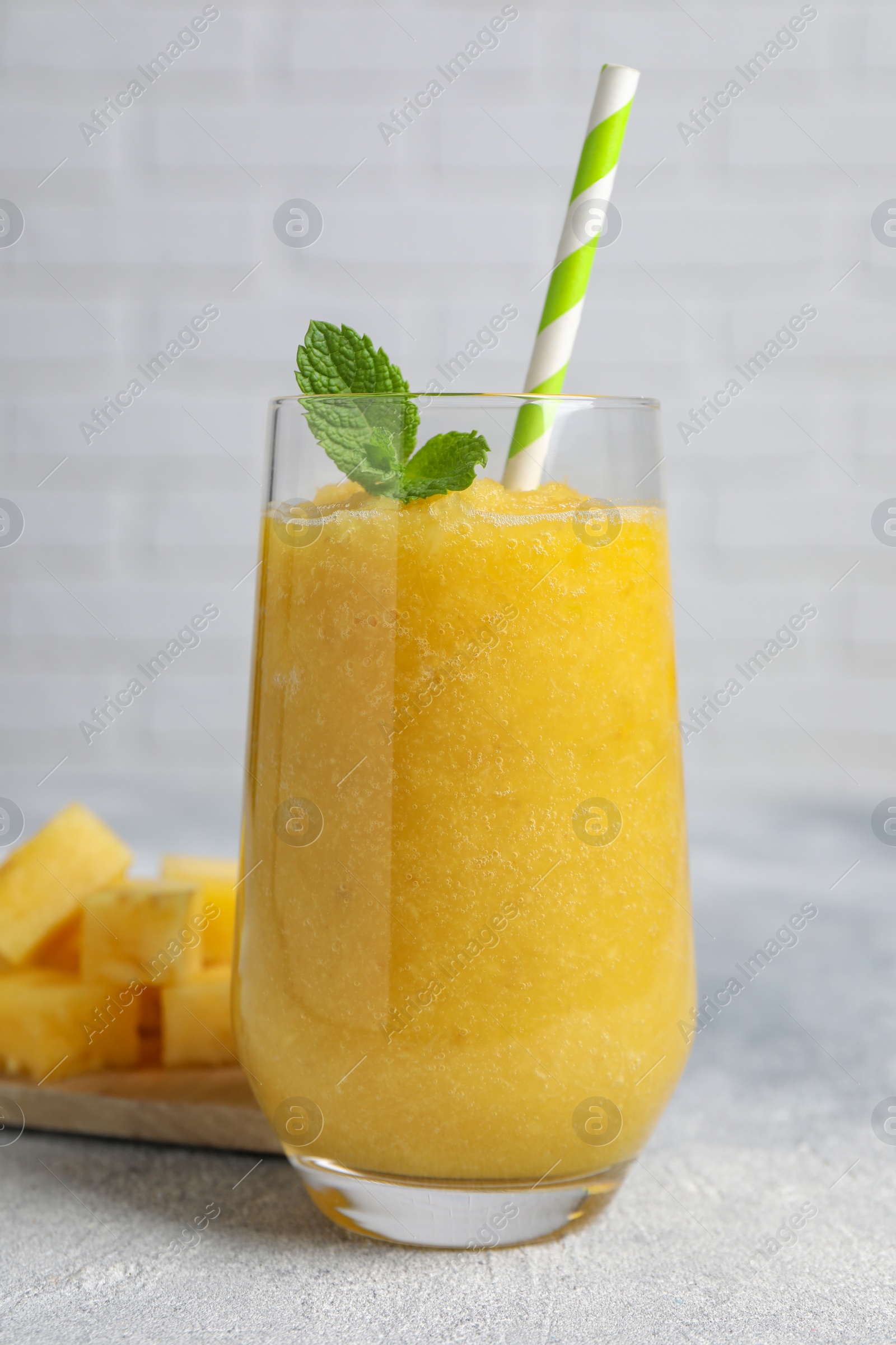Photo of Glass of tasty pineapple smoothie and cut fruit on light gray table