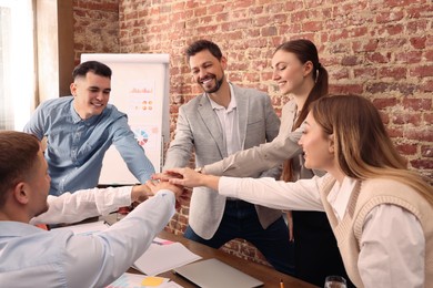 Photo of Office employees joining hands during meeting at work