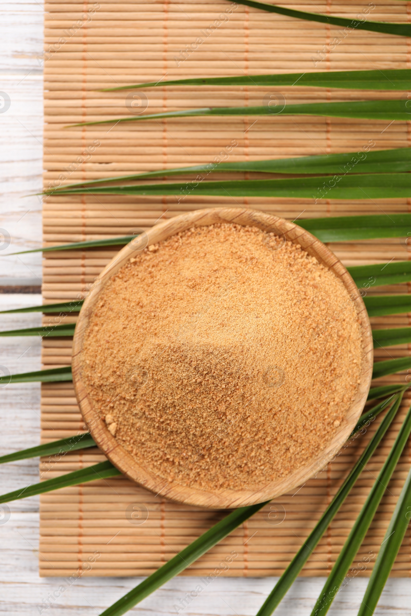 Photo of Coconut sugar, palm leaves and bamboo mat on wooden rustic table, top view