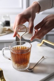 Photo of Woman pouring milk into cup of tea at white table, closeup