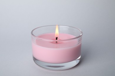 Burning candle in glass holder on light grey background