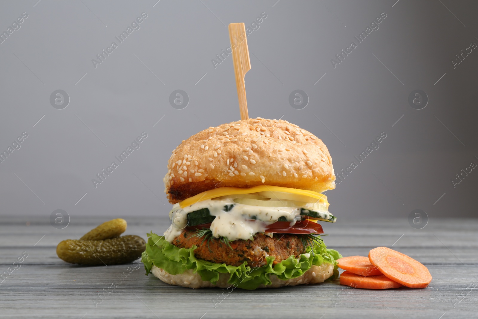 Photo of Delicious vegetarian burger and ingredients on grey wooden table