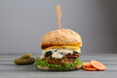 Photo of Delicious vegetarian burger and ingredients on grey wooden table