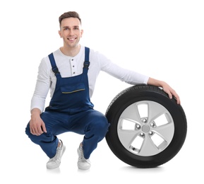 Male mechanic with car tire on white background