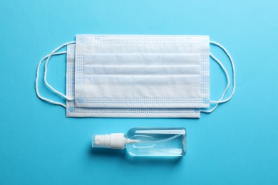 Protective masks and hand sanitizer on light blue background, flat lay. Safety equipment