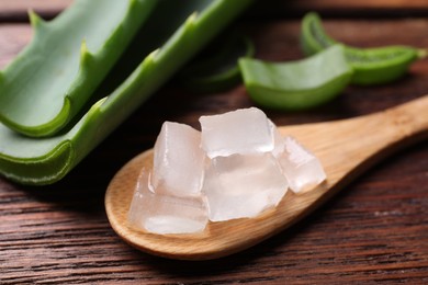 Photo of Aloe vera gel and slices of plant on wooden table, closeup