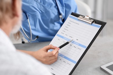 Photo of Doctor showing medical card to patient at table in clinic, closeup