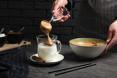 Woman making dalgona coffee at grey table, closeup