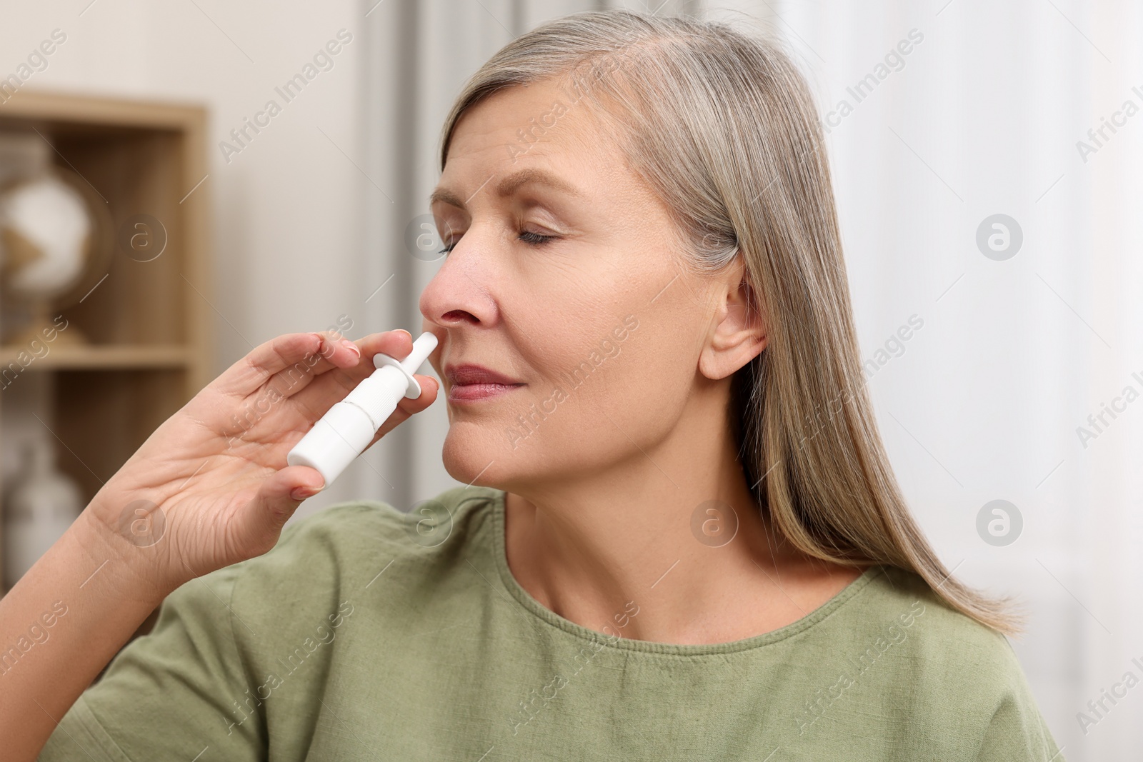 Photo of Medical drops. Woman using nasal spray indoors