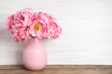 Beautiful bouquet of pink peonies in vase on wooden table. Space for text