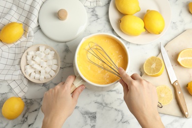 Photo of Woman cooking delicious lemon curd at white marble table, top view