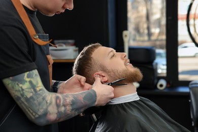 Photo of Professional hairdresser working with bearded client in barbershop