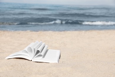 Open book on sandy beach near sea. Space for text
