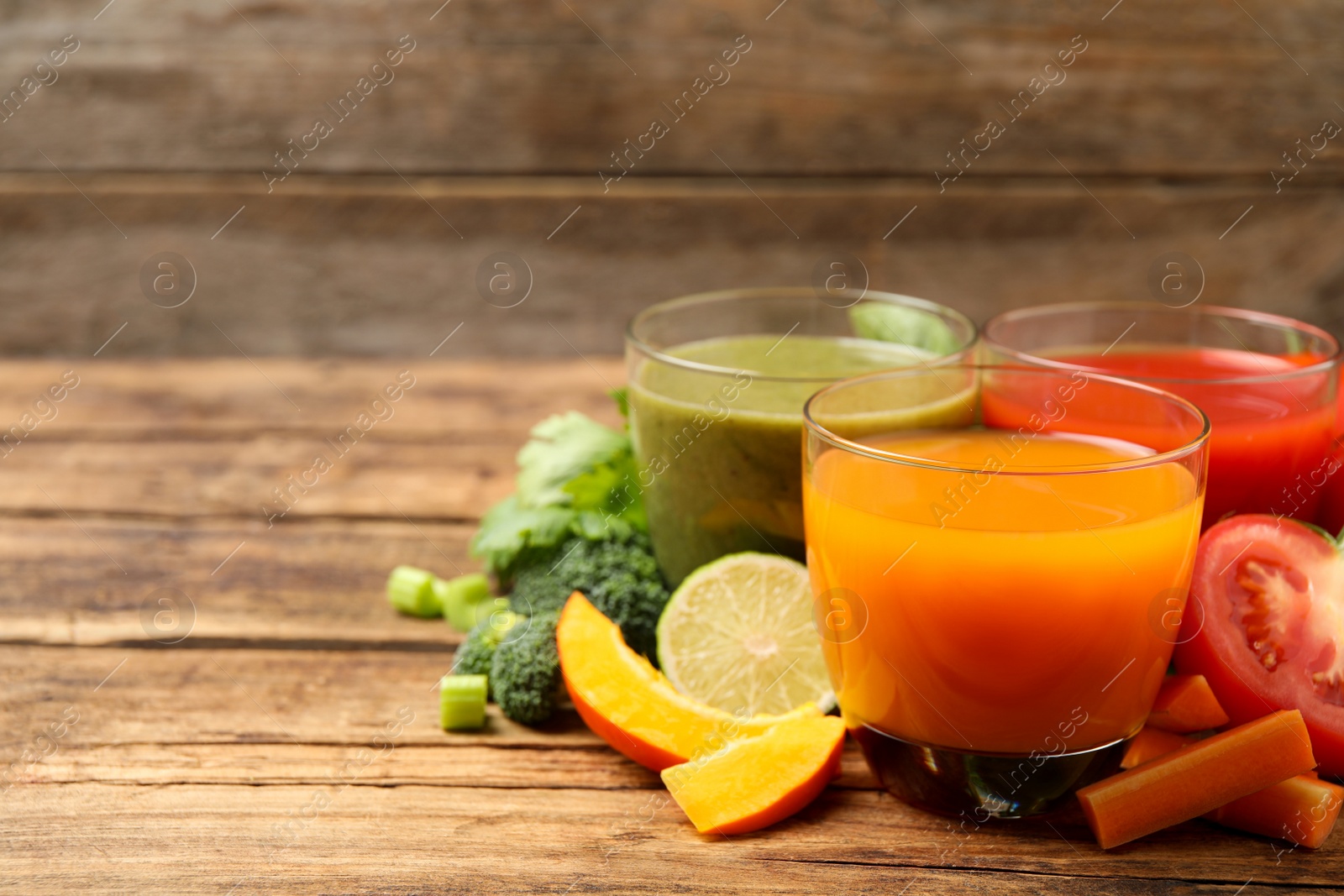Photo of Delicious vegetable juices and fresh ingredients on wooden table. Space for text