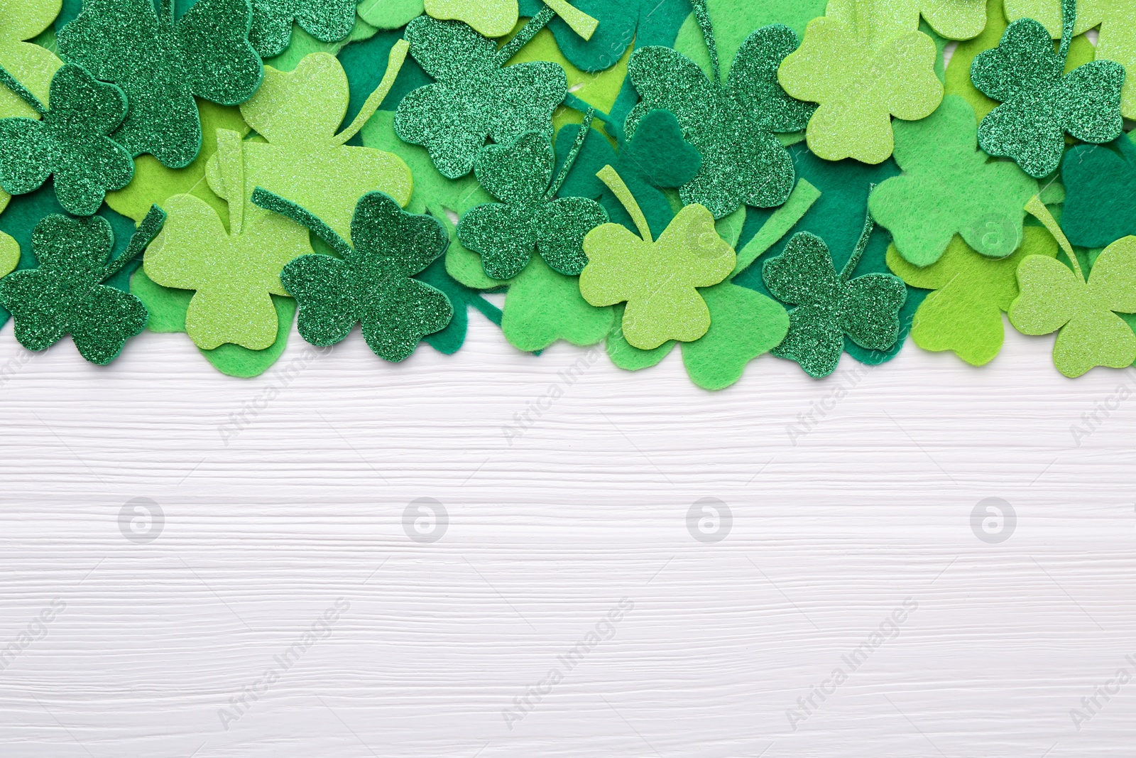 Photo of St. Patrick's day. Decorative green clover leaves on white wooden table, flat lay. Space for text