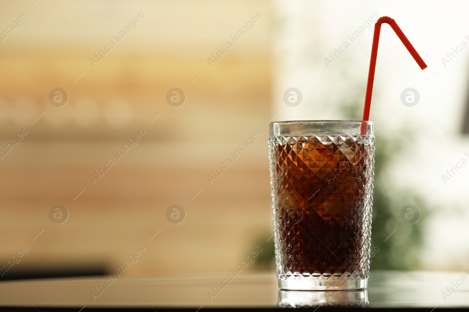 Photo of Glass of cola with ice on table against blurred background. Space for text