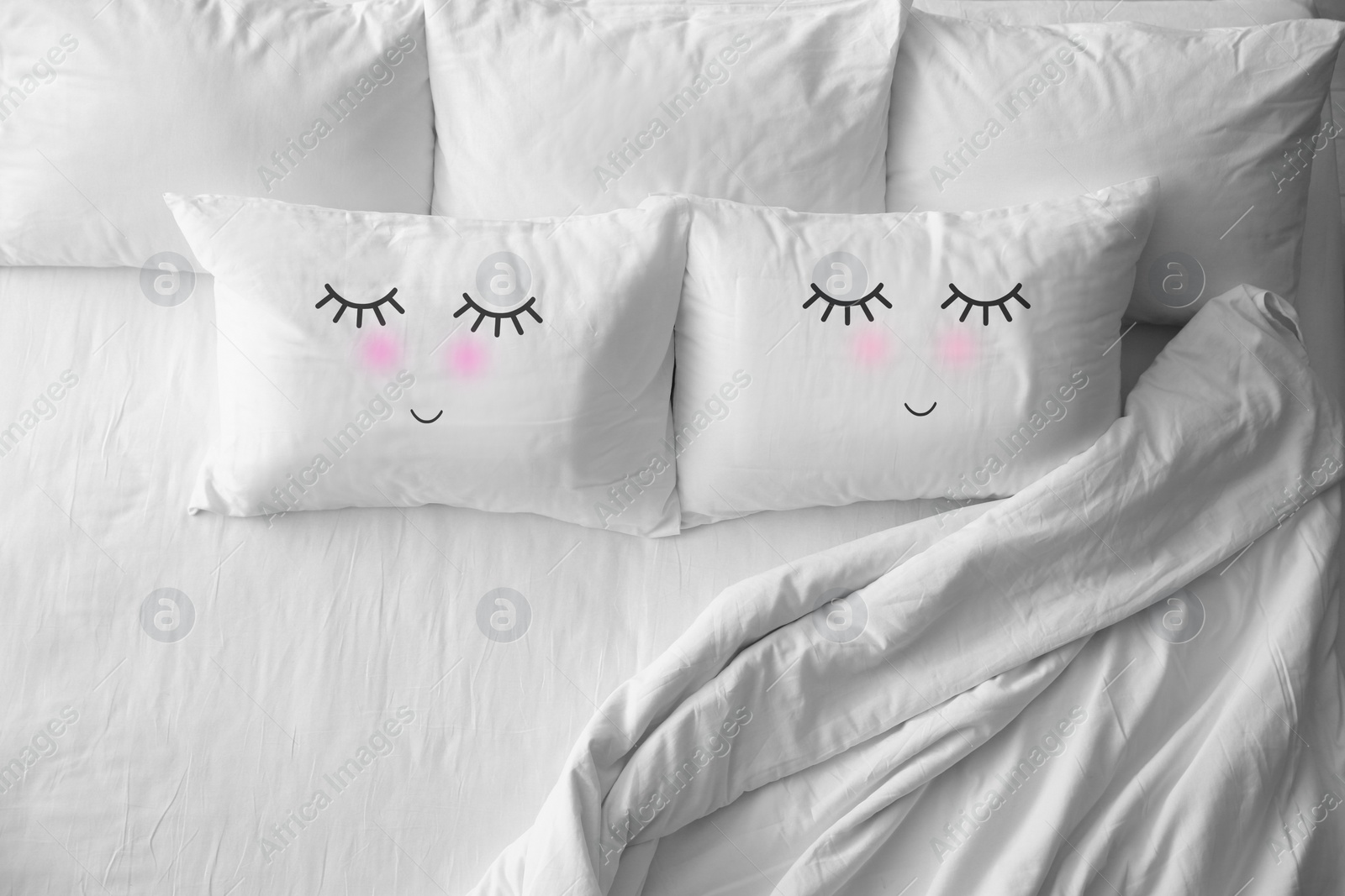 Image of Soft pillows with cute faces on comfortable bed, above view