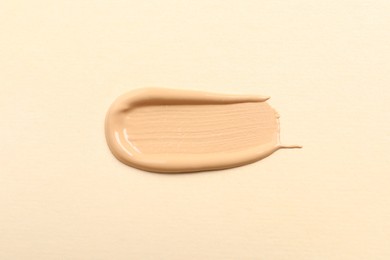 Photo of Smear of skin foundation on beige background, top view