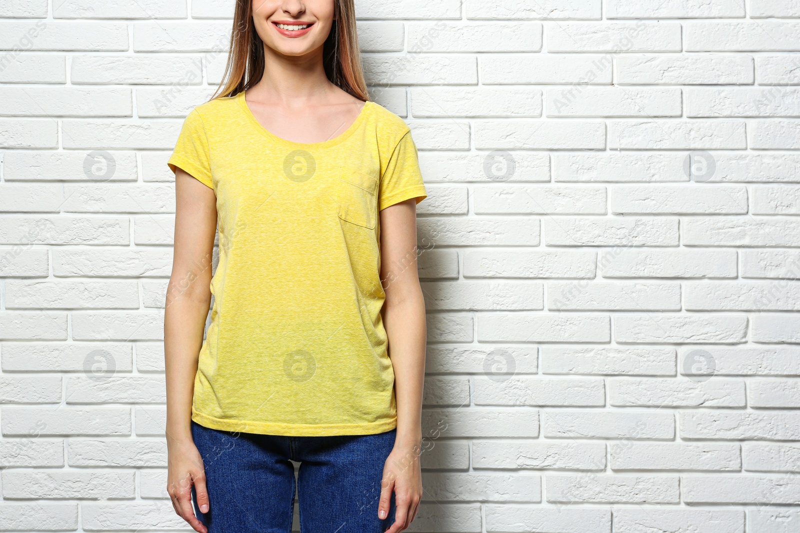 Photo of Young woman wearing blank t-shirt near white brick wall, closeup. Mockup for design