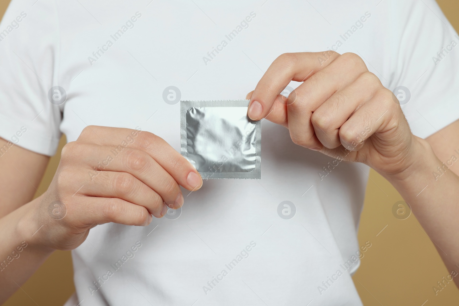 Photo of Woman holding condom on beige background, closeup. Safe sex