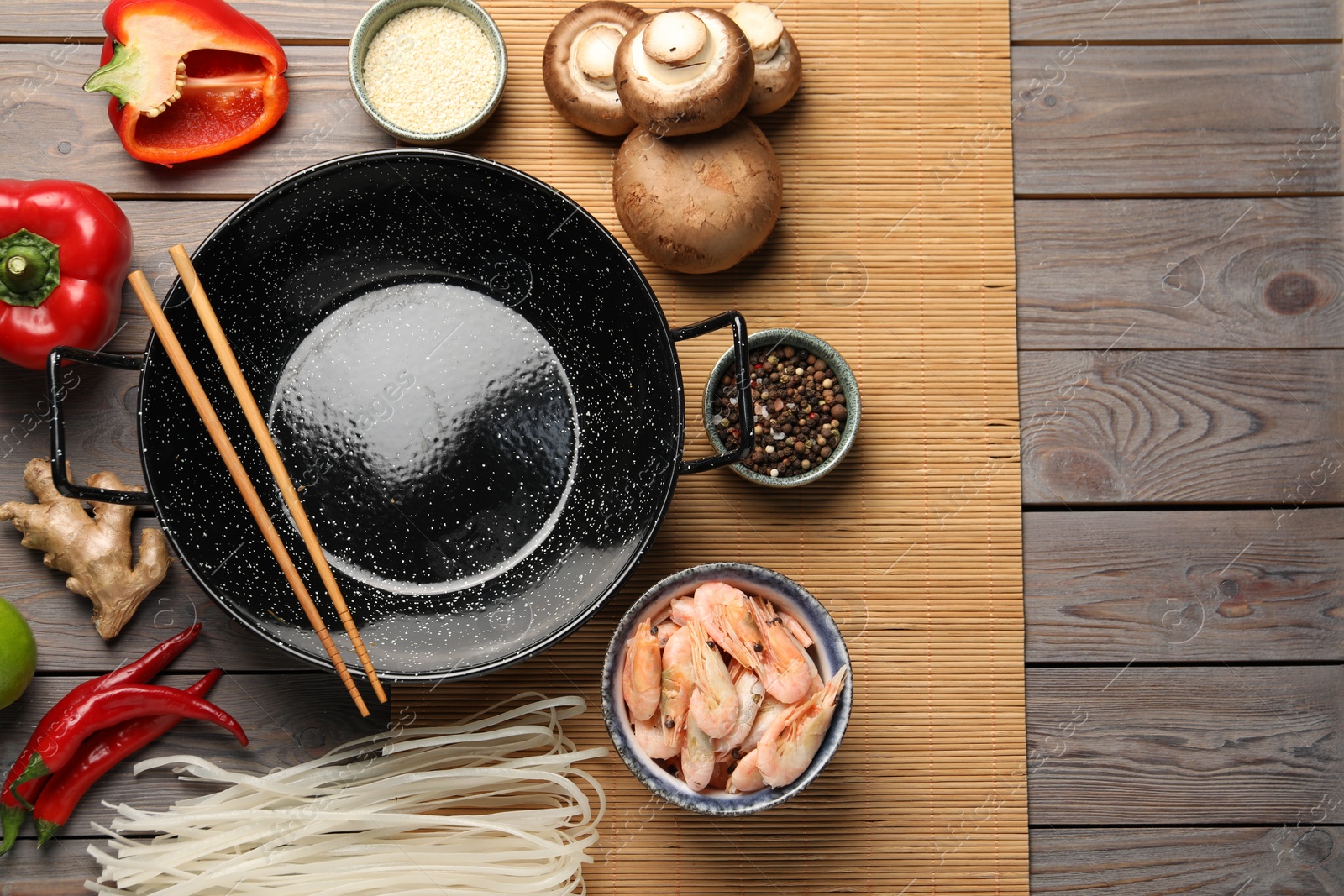 Photo of Black wok and chopsticks surrounded by products on color wooden table, flat lay