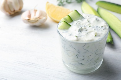 Photo of Glass bowl of Tzatziki cucumber sauce with ingredients on wooden background, space for text