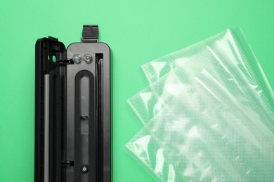 Photo of Sealer for vacuum packing with plastic bags on light green background, flat lay